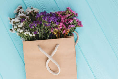 Different statice limonium flowers on paper bag. Blue wood background. Top view.の写真素材