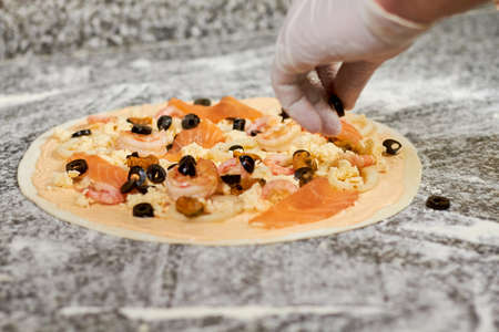 Adding black olives to pizza. Hand adding olive to uncooked pizza.の写真素材