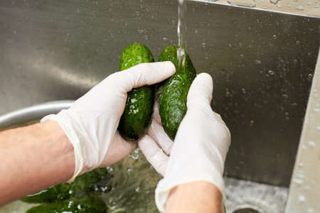 Chef washing cucumbers under tap water. Hands in white gloves washing two cucumbers.の写真素材
