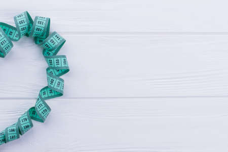 Twisted measuring tape with copy space. Measure tape on white wooden background with text space, cropped image.の写真素材
