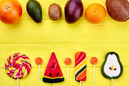 Various tropical fruits and candies. Exotic fruits set and lollipops on yellow wooden surface with text space. Healthy eating concept.の写真素材
