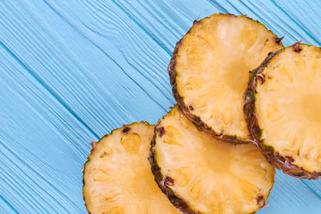 Fresh juicy pieces of ripe pineapple. Pineapple circles slices on blue wooden background and copy...