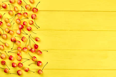 Border from ripe cherries and copy space. Group of cherries on yellow wooden background. Healthy and...