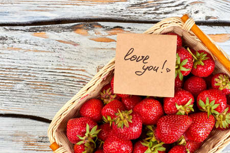 Basket of strawberries and Valentines Day card. Fresh juicy strawberries in wicker basket on vintage...