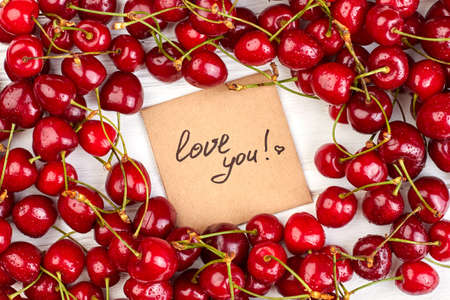 Valentines holiday background with fresh cherries. Close up ripe berries with water drops and paper card. Summer love confession.の写真素材