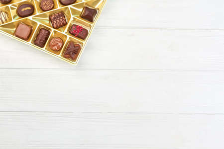 Different chocolate candies in box. Assortment of chocolate candies in golden box on white wooden...