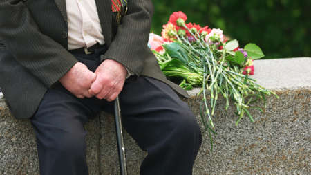 War veteran with stick sitting alone outdoors. Veteran received congratulation with Victory Day. Hero of Patriotic War. Hands of senior man. Victory Day celebration.の写真素材
