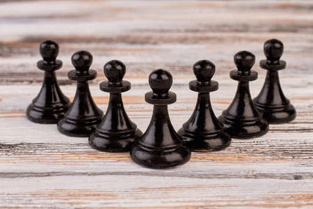Composition of black chess pawns. Set of black chess pieces on light wooden background. Playing...