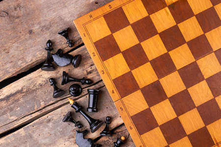Brown chess board and black chess figures. Chess pieces lying near game board on rustic wooden...