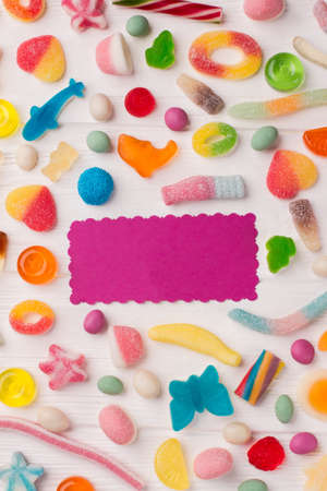 Tasty colorful candies on wooden background. Background of multicolored candies with blank paper card.の写真素材