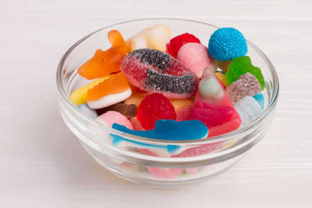 Glass bowl full of colorful candies. Many multicolored marmalade sweets in glass vase on white...