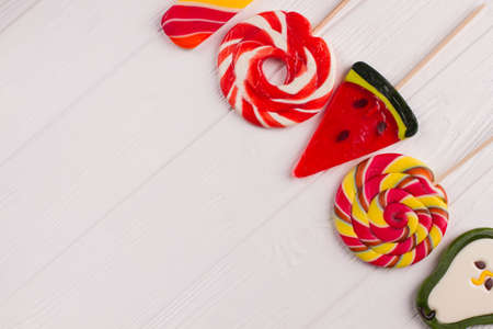 Colorful candies on white wooden background. Large lollipops in a shape of pear, watermelon and...