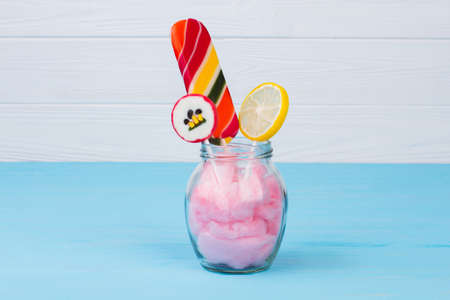 Glass jar with colorful lollipops on wooden background. Glassware with candies on color background....