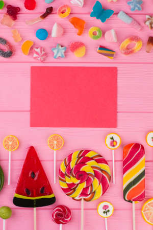 Blank card and colorful candies. Flat lay assorted sweets on pink wooden background. Greeting card background.の写真素材
