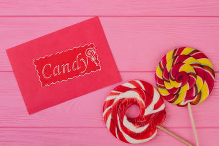 Composition with colorful lollipops on pink background. Two delicious lollipops and card with inscription Candy on color wooden background.の写真素材