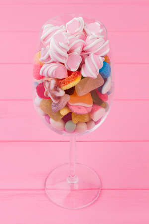 Various candies in wine glass. Transparent glass full of colorful candies and sweets on pink...