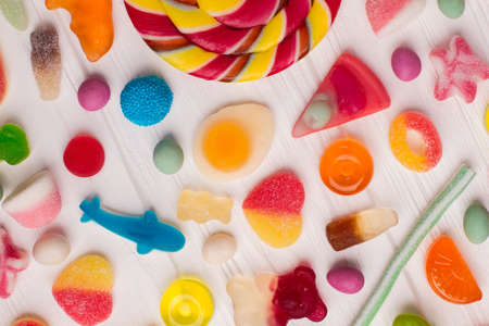 Colorful sugar candies on white wooden background. Sweets of different colors and shapes close up....
