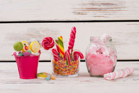 Glass jars with colorful candies, lollipops and gum balls. Composition of different candies on wooden background.の写真素材