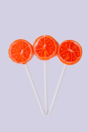 Three lollipops in a shape of oranges. Composition from candies on sticks, vertical image.の写真素材