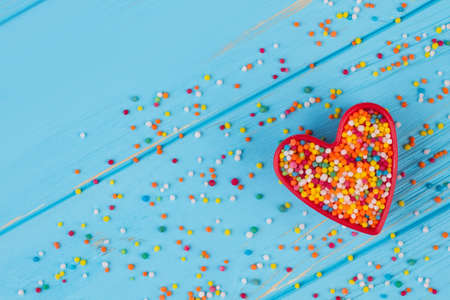 Cookie cutter with candy sprinkles, top view. Multicolored candy sprinkles on blue wooden background. Happy Valentines Day.の写真素材