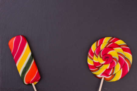 Two different lollipops on dark background. Black background with multicolored candies on sticks with copy space. Kids Birthday greeting card.の写真素材