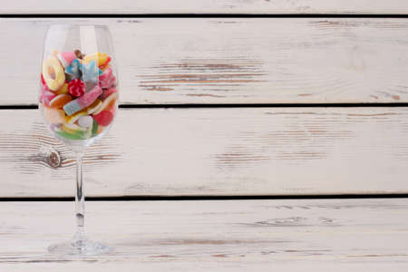 Wine glass filled with different colored candies. Colorful sweets in wine glass on wooden background with copy space. Holiday decoration with sweets.の写真素材