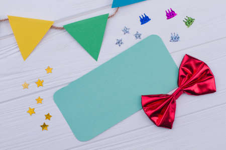 Birthday accessories on white wooden background. Birthday party items including paper flags, blank card, confetti and red bow-tie.の写真素材