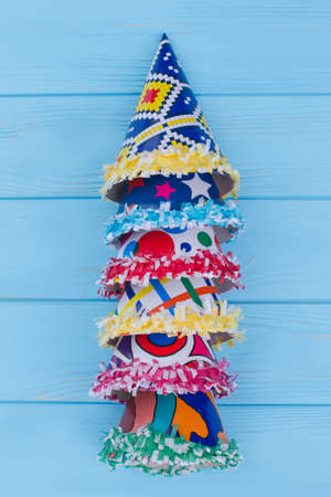 Row of party hats, vertical image. Set of different Birthday caps on color wooden background, top view. Kids accessories for party celebration.
