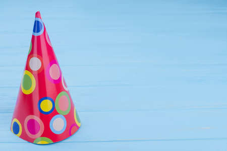 Birthday party paper cone hat. Kids party cap on color wooden background with text space.