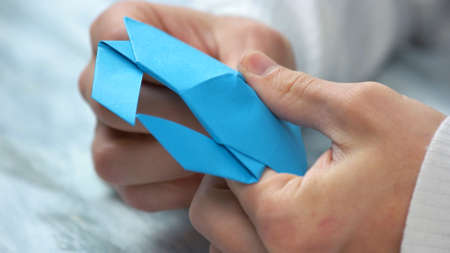 Close up male hands folding origami figure. Man making origami from blue paper. Paper folding art.
