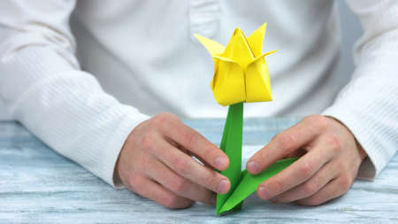Male hands holding yellow origami tulip. Beautiful spring flower made from paper. Handmade gift for Womens or Mothers Day.の写真素材