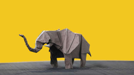 Origami elephant on yellow background. Animal figure made of wet-folding technique. Handcrafting...