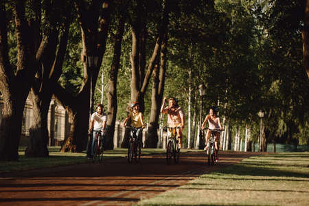 Joyful people on bikes, front view. Cute group of students biking in park. Youth and healthy way of...