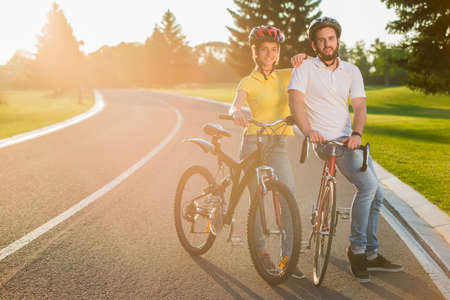 Happy cheerful couple with bikes outdoors. Beautiful couple of students enjoying sunny day riding...