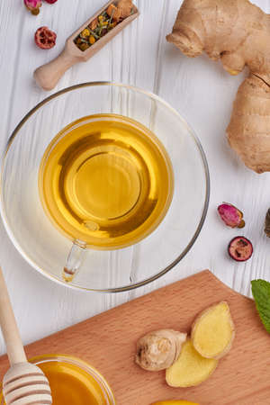 Cup of tea and seasoning, top view. Glass cup of ginger tea, ginger root, honey, dried tea and green...