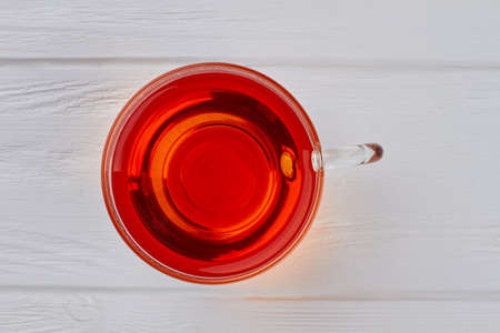 Glass cup with black tea, top view. Transparent mug of tea on white wooden background. Delicious and...