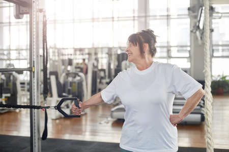 Elderly woman training hand at gym. Suspension training for older adults.