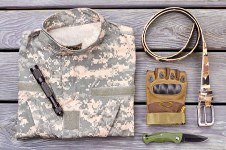 Military jacket and accessories. Torch, glove, belt and knife on wood.