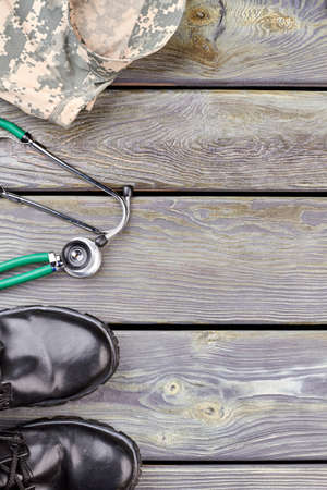 Camouflage jacket, stethoscope and black shiny shoes. Wooden desk background.の写真素材