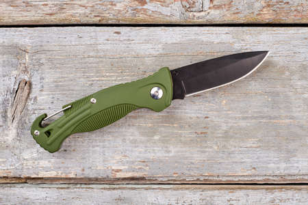 Army pocket knife with green handle. Wooden desk background. Top view.