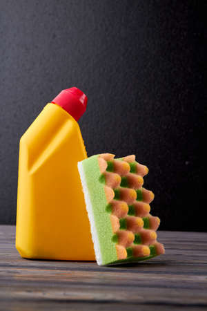 Detergent in yellow bottle and sponge. Plastic bottle with cleaning liquid on dark background. Household chores concept.の写真素材