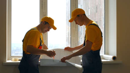Construction workers looking at blueprint. Two young builders discussing plan of work at new...