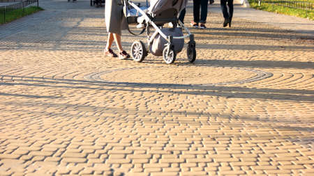 Woman with a stroller walking in the park. Cobblestones surface. People walking outdoor on a sunny day.の写真素材