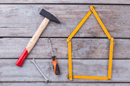 Construction tools on vintage wooden background. Hammer, screwdriver, spanner and folding ruler in a shape of house.の写真素材
