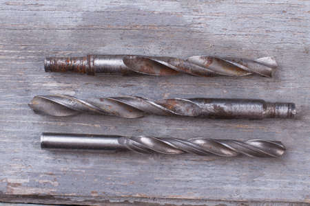 Three rusty drills on wooden background. Set of used drill bits for metal, wood and other materials.