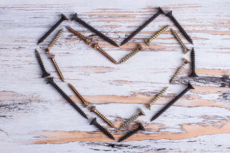 Heart shape from black and golden screws. Metal tools forming heart shape on wooden boards. Love and romance.の写真素材