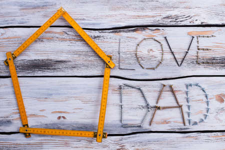 LOVE DAD text on wooden background. Folding ruler in a shape of house and inscription LOVE DAD. Flat...