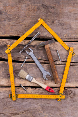 Different hand tools for construction on rustic background. Folding ruler in a shape of house and various carpentry tools on wooden boards.の写真素材