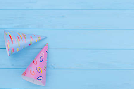 Two party hats on color wooden boards. Blue and pink Birthday caps on blue wooden background with copy space. Birthday greeting background.の写真素材