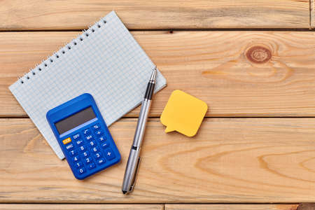 Office supplies on wooden background. Sticky note, calculator, notebook, ballpoint pen. Business and work concept.の写真素材